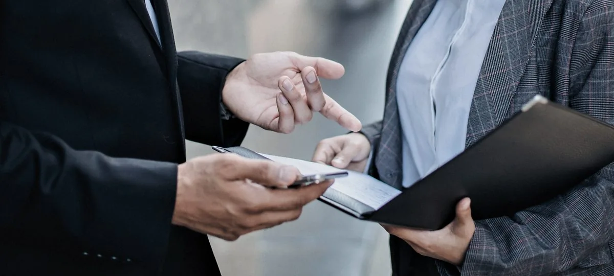 Detalhe de duas pessoas conferindo um extrato sobre um celular